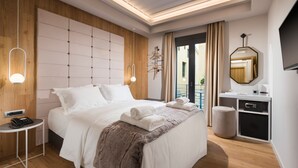Una camera d'albergo moderna con un letto grande, un comodino con il telefono, un poggiapiedi rotondo, una scrivania con uno specchio e una TV a parete.