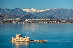 A historic castle on a small island in a calm lake, surrounded by mountains and a town in the background.