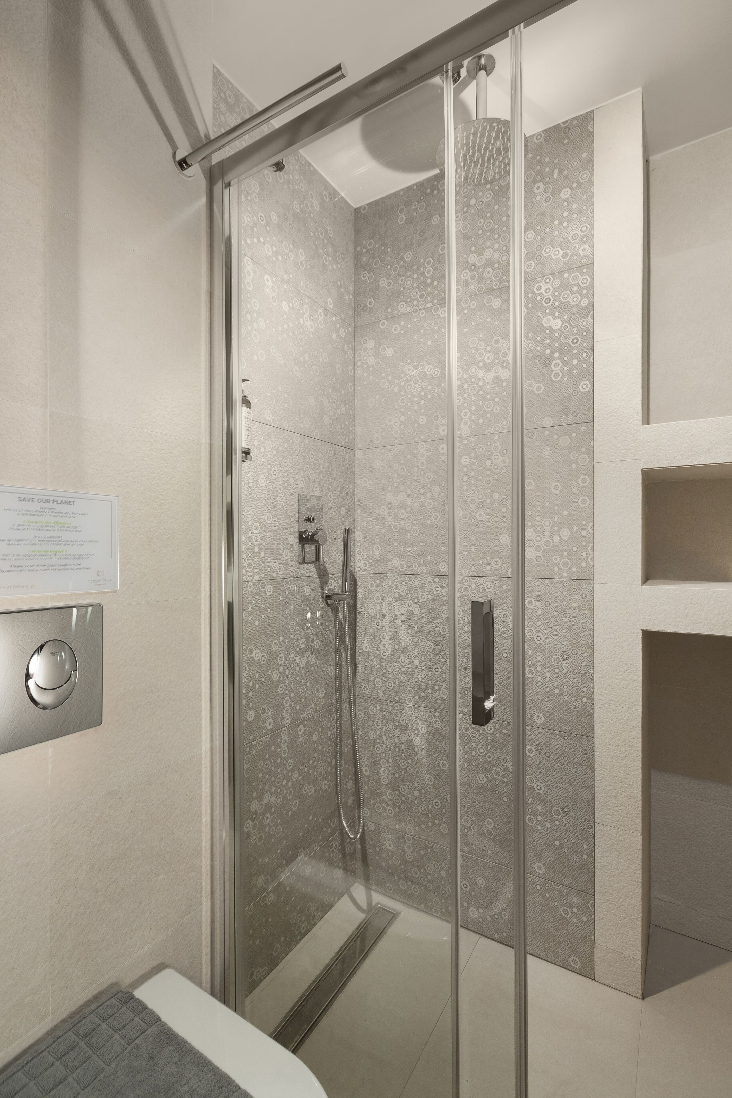 A modern shower with a glass door, a wall-mounted control panel, and a "SAVE OUR PLANET" sign.