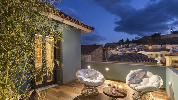 Una terrazza sul tetto con due poltrone bianche imbottite, un tavolino con candele e vista sulla città al crepuscolo.