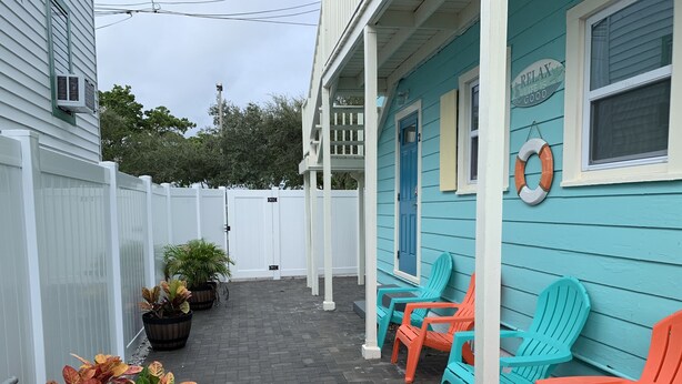 A porch with outdoor seating, a white fence, and potted plants.