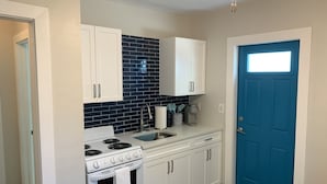 A compact kitchen with white cabinets, a black tiled backsplash, a stove, and a sink.