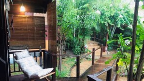 A wooden deck with a cushioned chair, surrounded by lush greenery and a wooden staircase leading to a higher level. - La Case Bois Creole (COCO) (Albion)