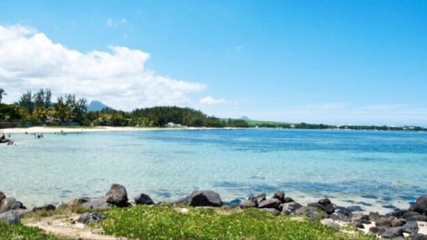 A coastal landscape with clear blue water, rocky shoreline, and a distant forested area. - La Case Bois Creole (COCO) (Albion)