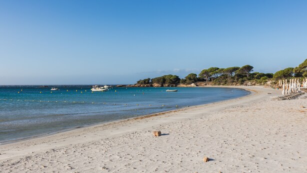 Una spiaggia con acqua cristallina, una costa sabbiosa e barche all'orizzonte.