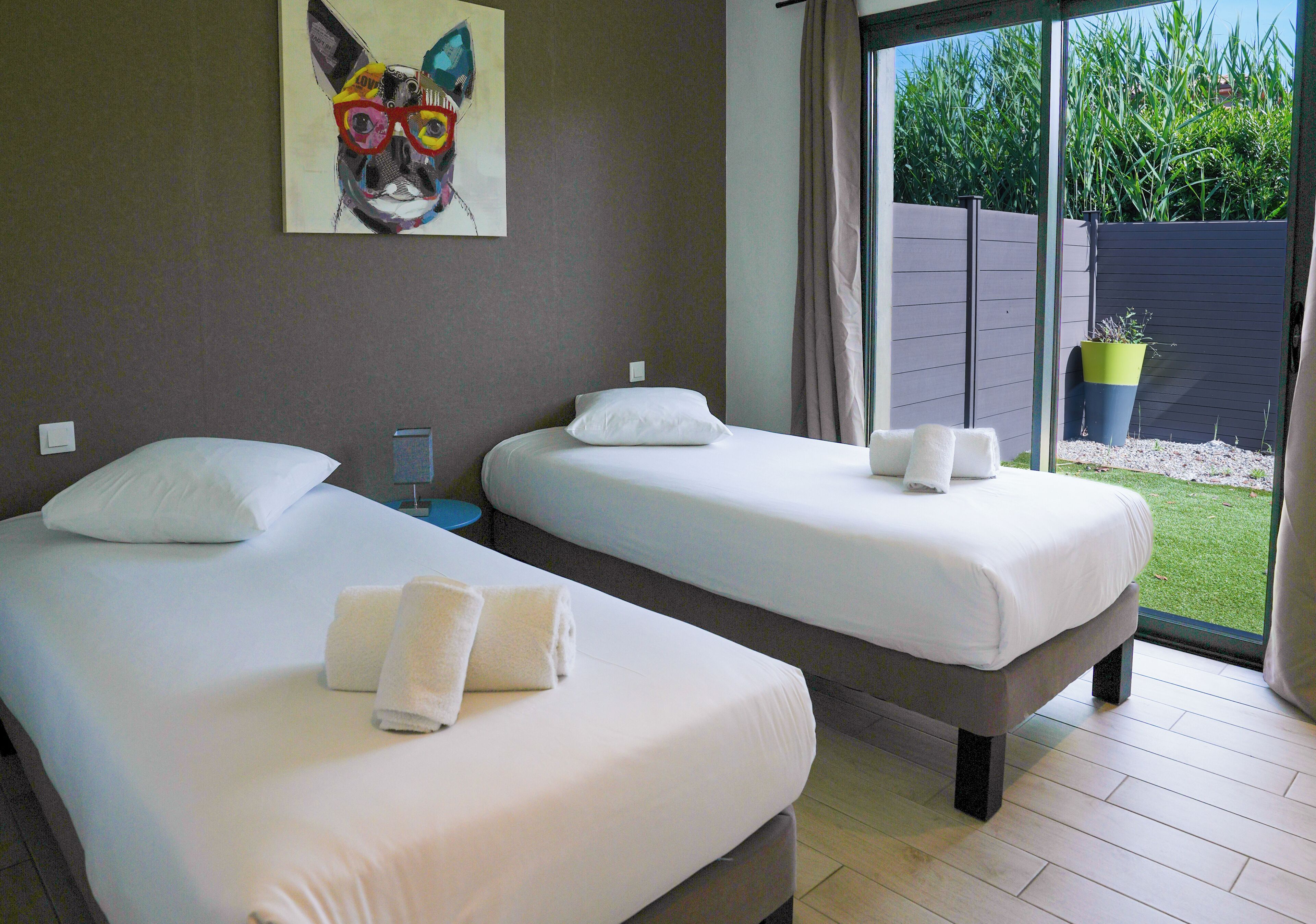 A hotel room with two beds, a painting on the wall, and a view of the outdoors.
