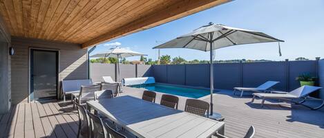 A covered outdoor area with a pool, lounge chairs, and a table with chairs.
