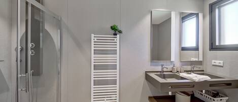 A modern bathroom with a glass shower enclosure, a white towel rack, a sink with a mirror, and a window providing natural light.