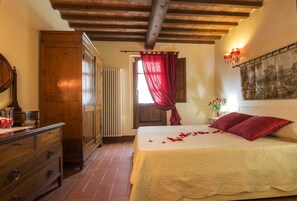A bedroom with a wooden wardrobe, a radiator, a bed with red pillows, and a painting on the wall. - Villa del Poggetto (Terranuova Bracciolini)