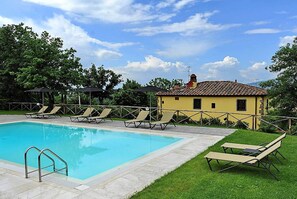 A swimming pool with lounge chairs and umbrellas, surrounded by a grassy area and a yellow building with a tiled roof. - Villa del Poggetto (Terranuova Bracciolini)