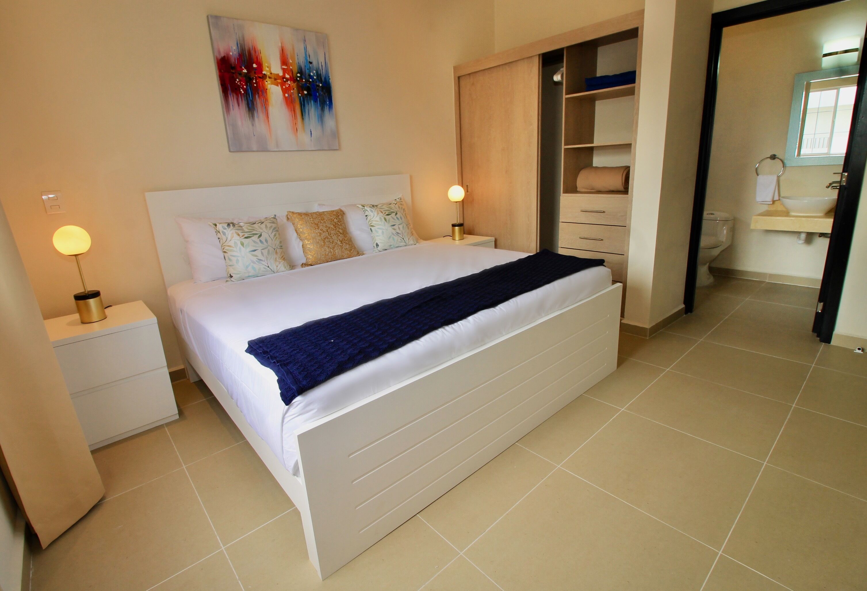 A neatly arranged bedroom with a large bed, bedside tables, a wardrobe, and a bathroom visible through an open door.