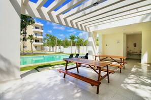 Relax by the pool surrounded by lush greenery and shaded by a pergola.