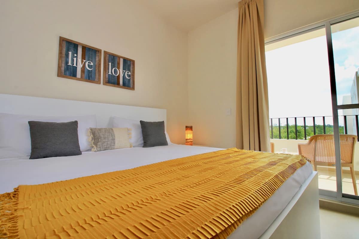 Una habitación de hotel con una cama grande, un balcón con mobiliario de mimbre y vistas a la ciudad.