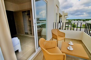 A balcony with wicker chairs and a table, a sliding glass door, and a view of buildings and greenery.