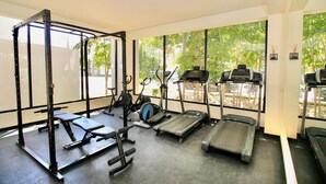 Une salle de sport équipée d’un support à squats, d’un banc de développé couché, d’un appareil elliptique et de tapis de course.