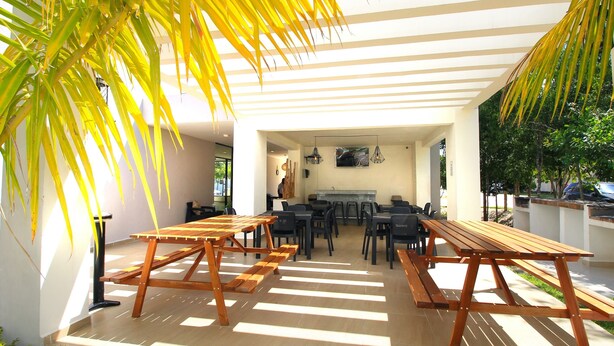 Une terrasse extérieure avec des tables et des chaises en bois, un espace salon couvert et une vue sur la rue.