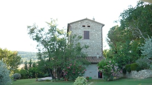 A stone building with a small window and a door, surrounded by a well-maintained garden with various plants and flowers. - Casale Luigina (Monte Castello di Vibio)