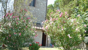 A stone building with a tiled roof, surrounded by lush greenery and flowering plants. - Casale Luigina (Monte Castello di Vibio)