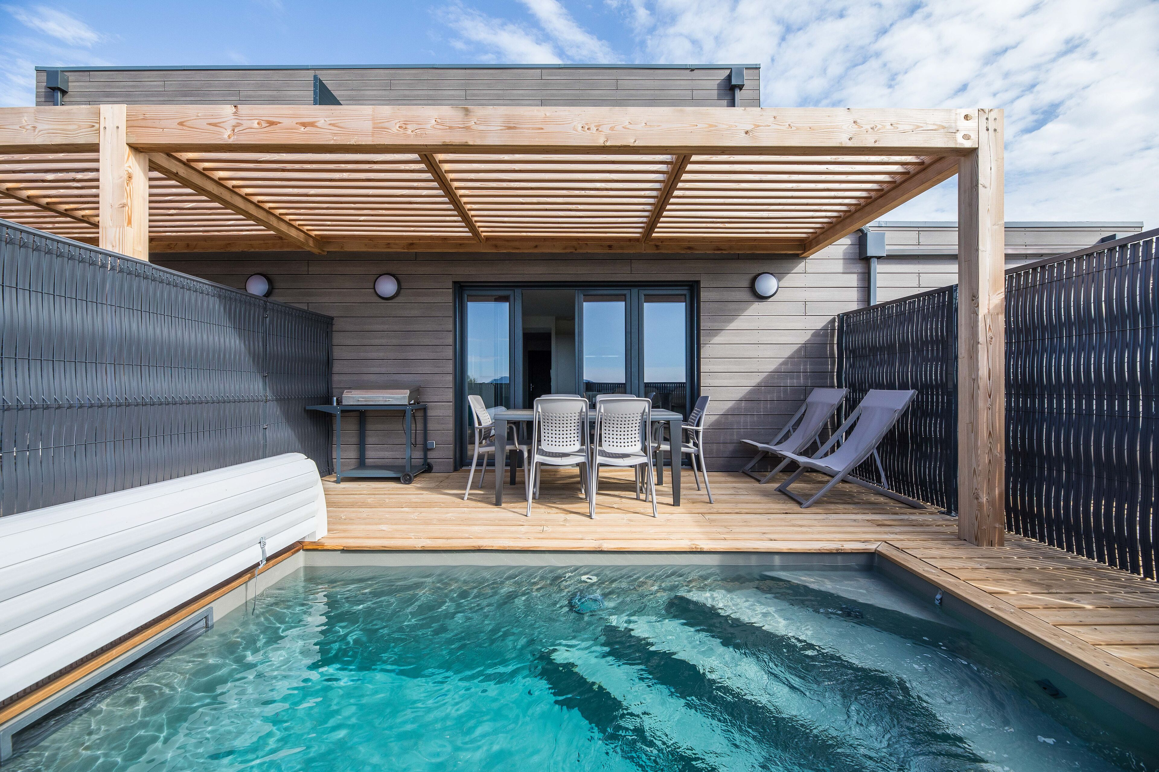 Un área de piscina con terraza de madera, sillas de descanso y una zona de estar cubierta.