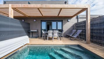 Un área de piscina con terraza de madera, sillas de descanso y una zona de estar cubierta.