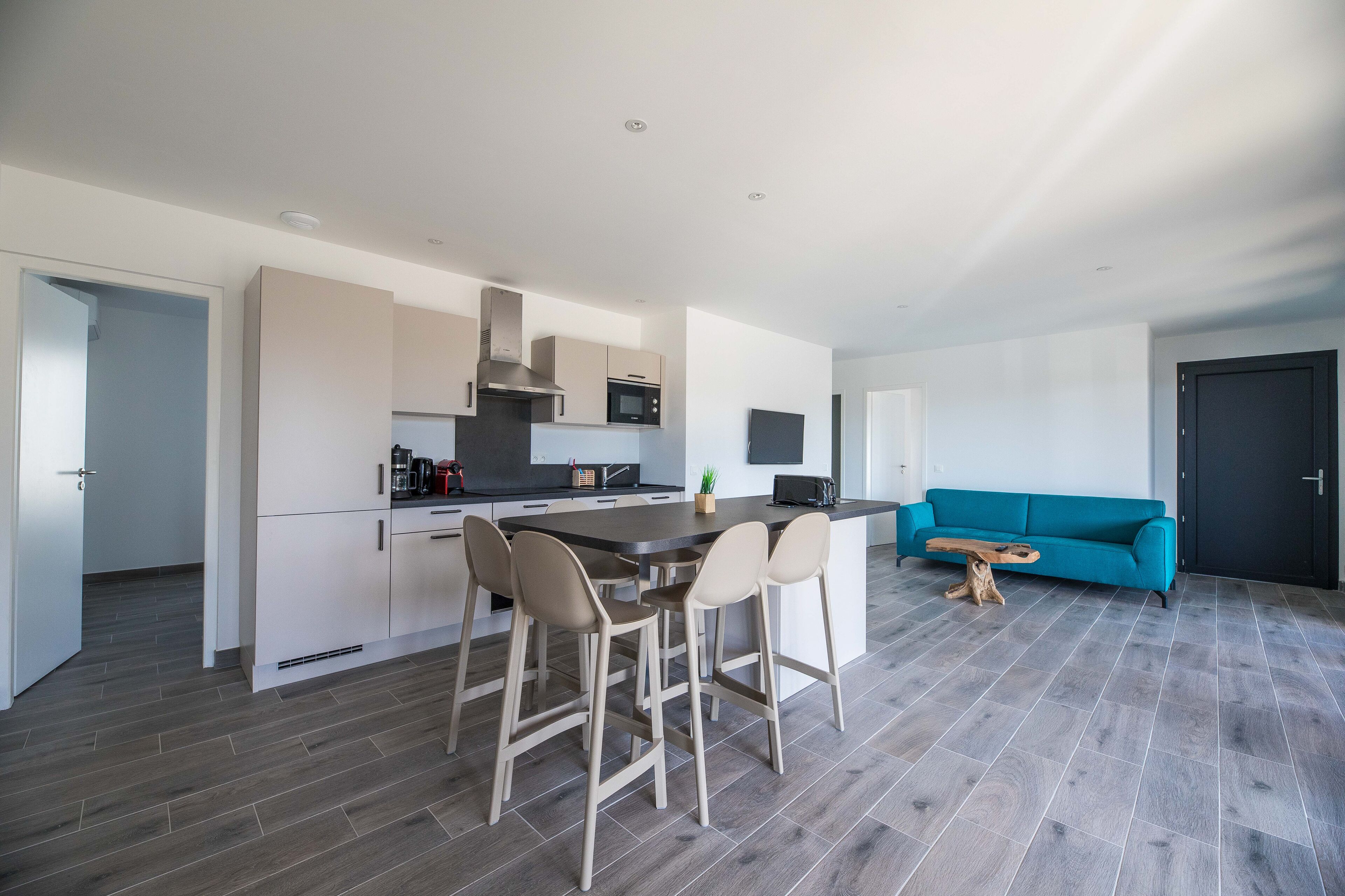 Et moderne køkken med en central ø, barstole og en teal sofa i en stue.