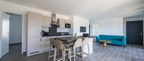 Et moderne køkken med en central ø, barstole og en teal sofa i en stue.