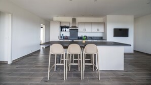 Eine moderne Küche mit einer zentralen Kochinsel, Barhocker und einem an der Wand befestigten Flachbildfernseher.