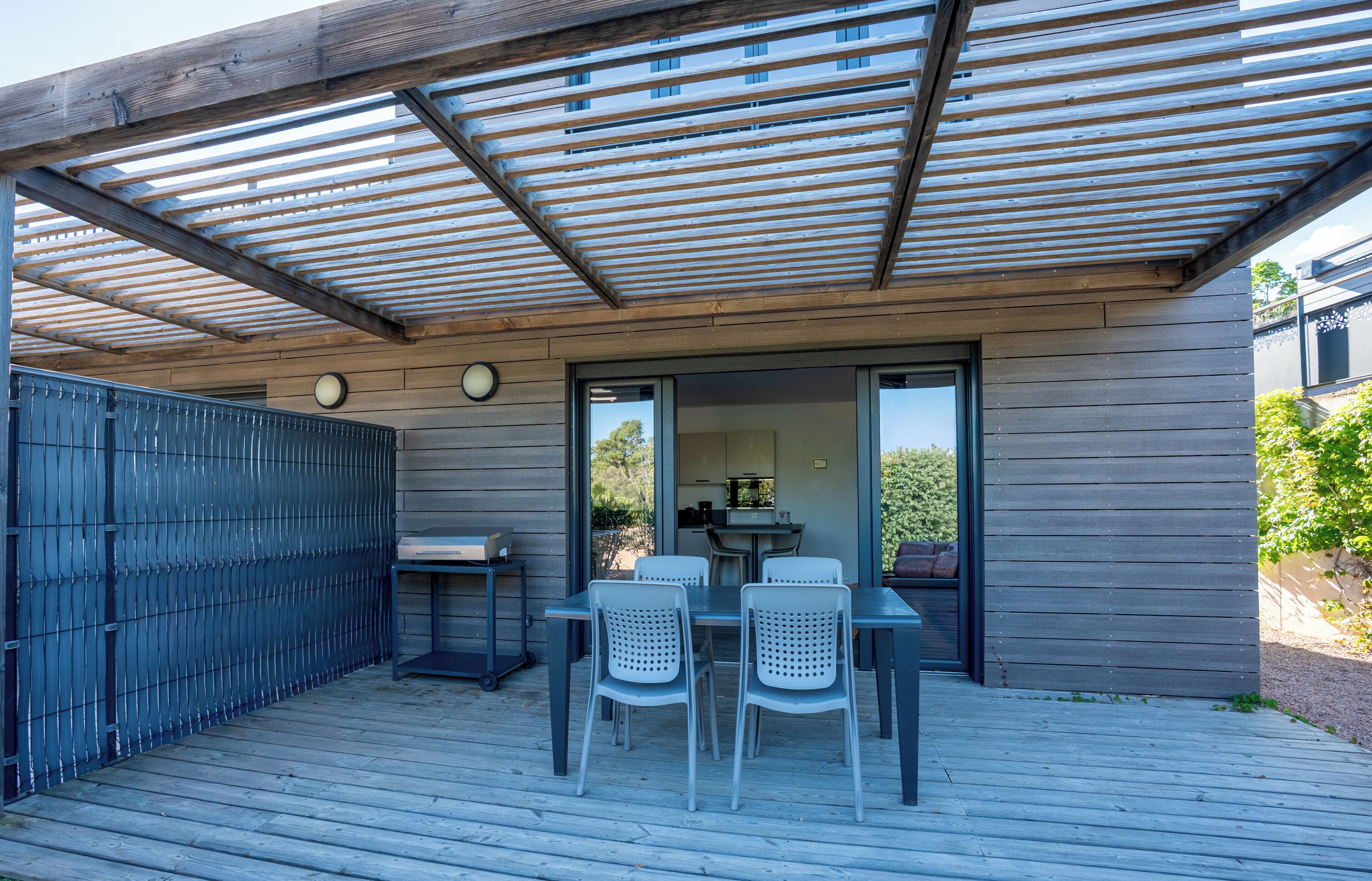 A covered patio with a table and chairs, a grill, and a view of the outdoors.