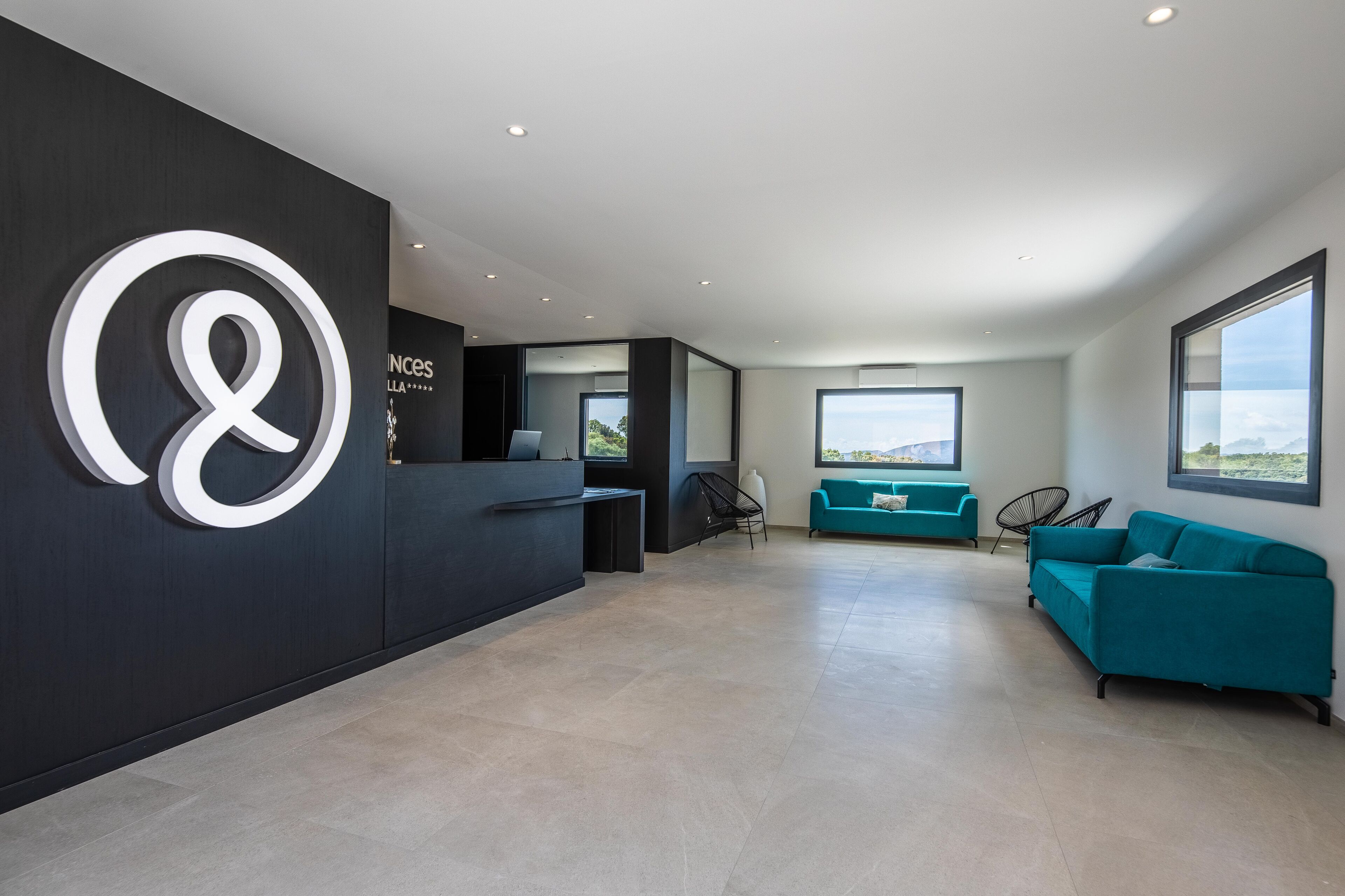 A modern reception area with a large logo, a reception desk, teal sofas, and large windows offering views.