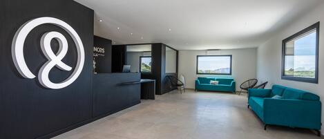 A modern reception area with a large logo, a reception desk, teal sofas, and large windows offering views.