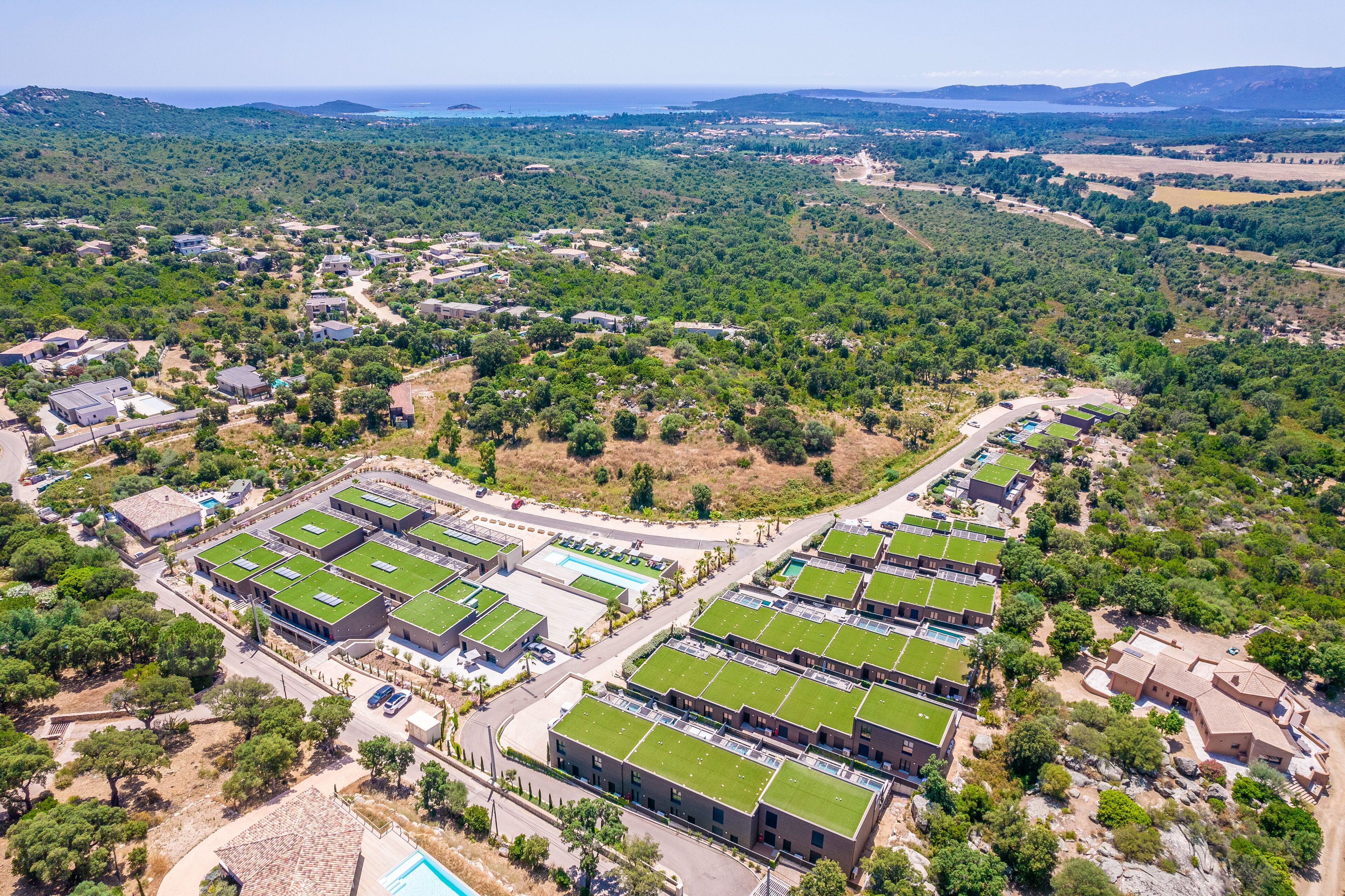 Vista aérea de un resort con varias edificaciones con techos verdes, rodeado de exuberante vegetación y un paisaje montañoso.