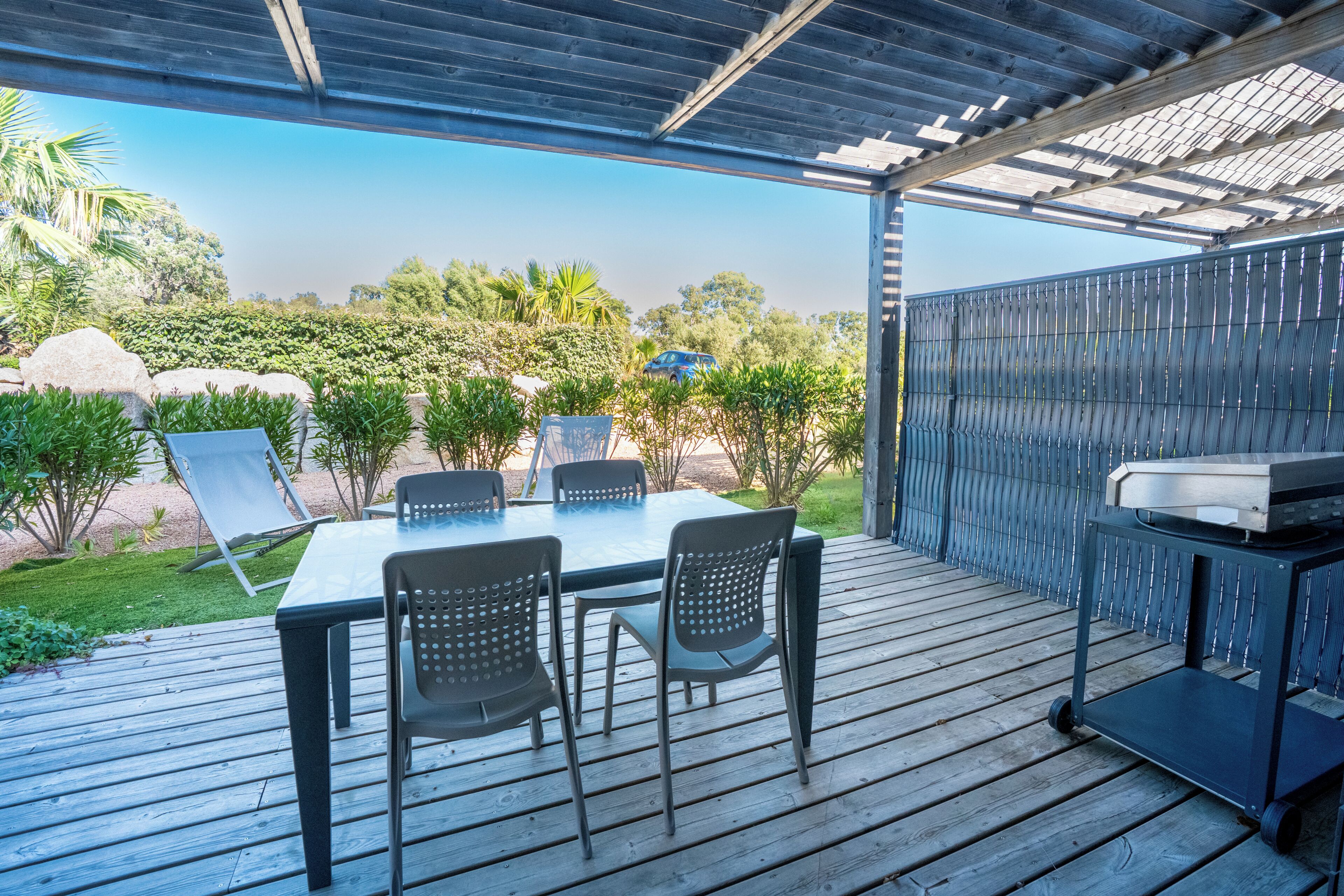 An outdoor patio with a table and chairs, a grill, and a view of the surrounding landscape.