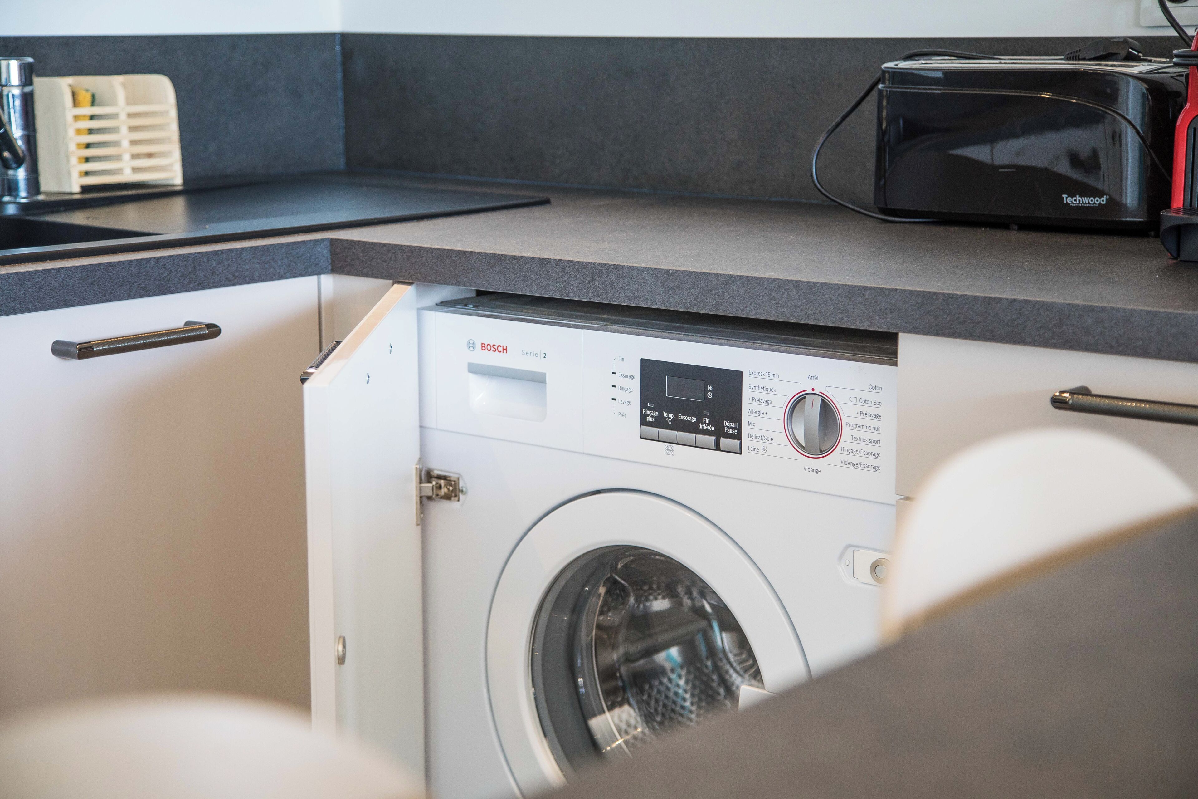 Une cuisine compacte équipée d’un lave-linge Bosch, d’un grille-pain et d’un évier.