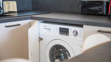 Een kleine keuken met een Bosch wasmachine, een broodrooster en een spoelbak.