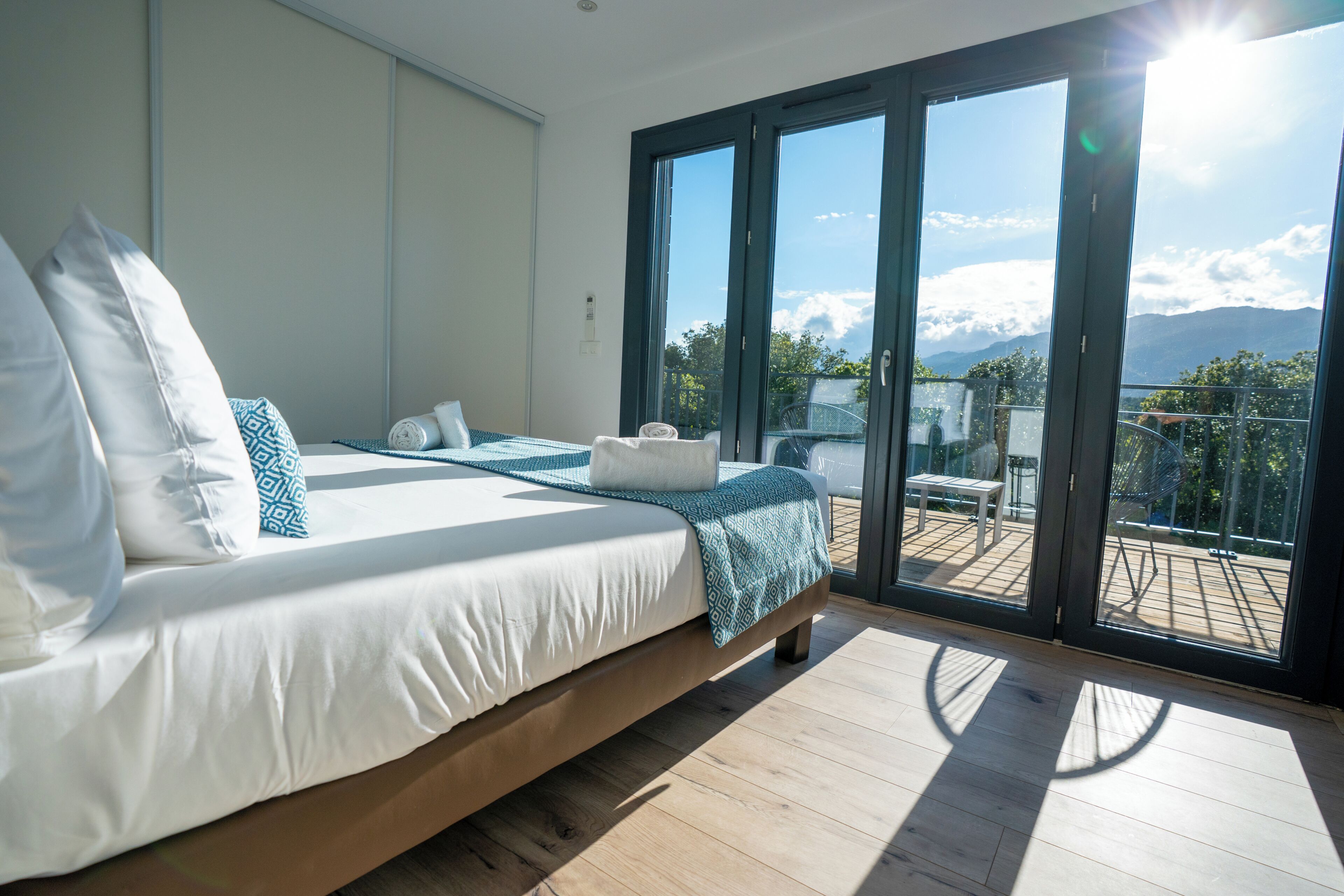 Quarto com cama grande, varanda com vista para montanhas e porta de vidro deslizante.