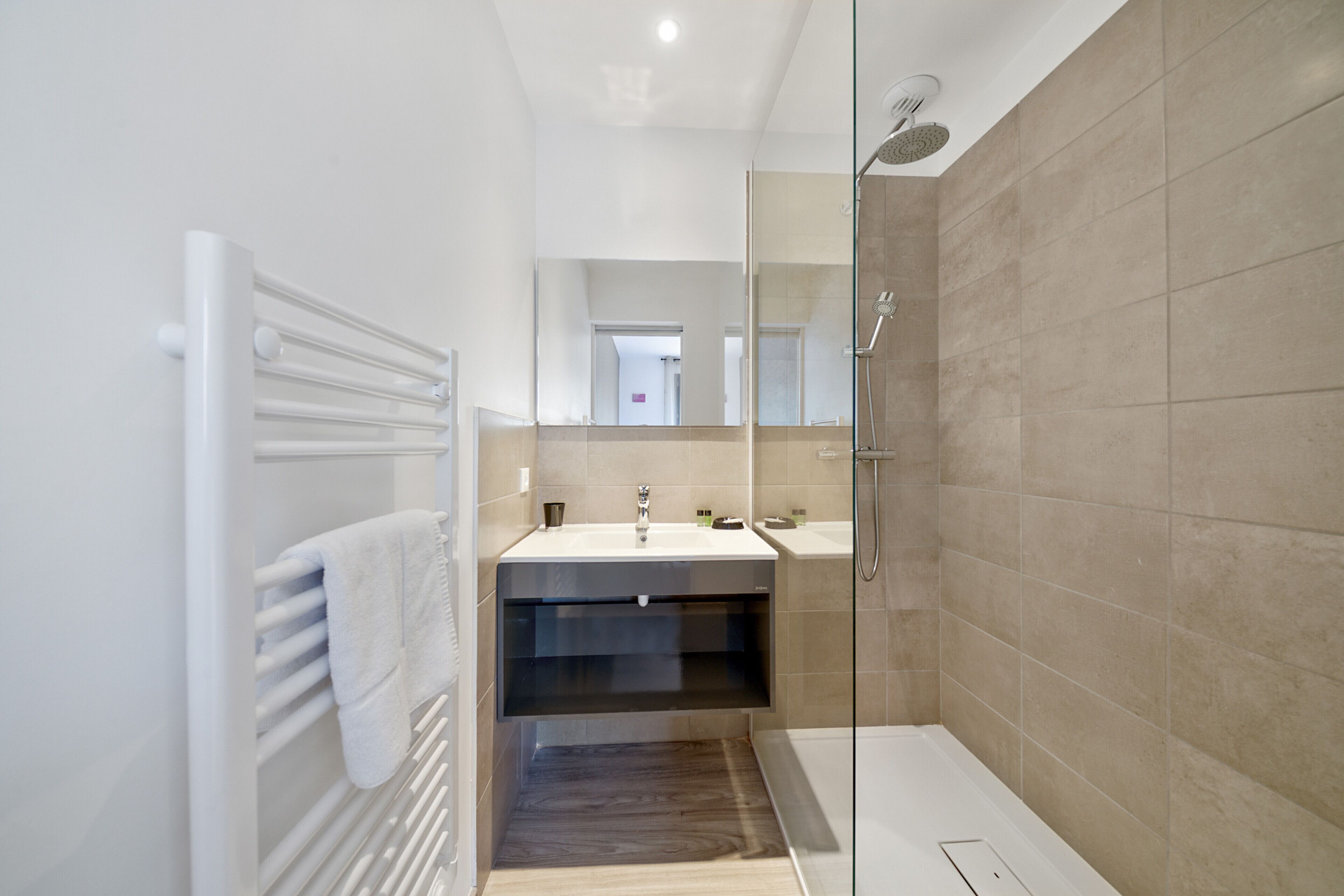 A modern bathroom with a glass shower enclosure, a white sink, and a dark wood floor.