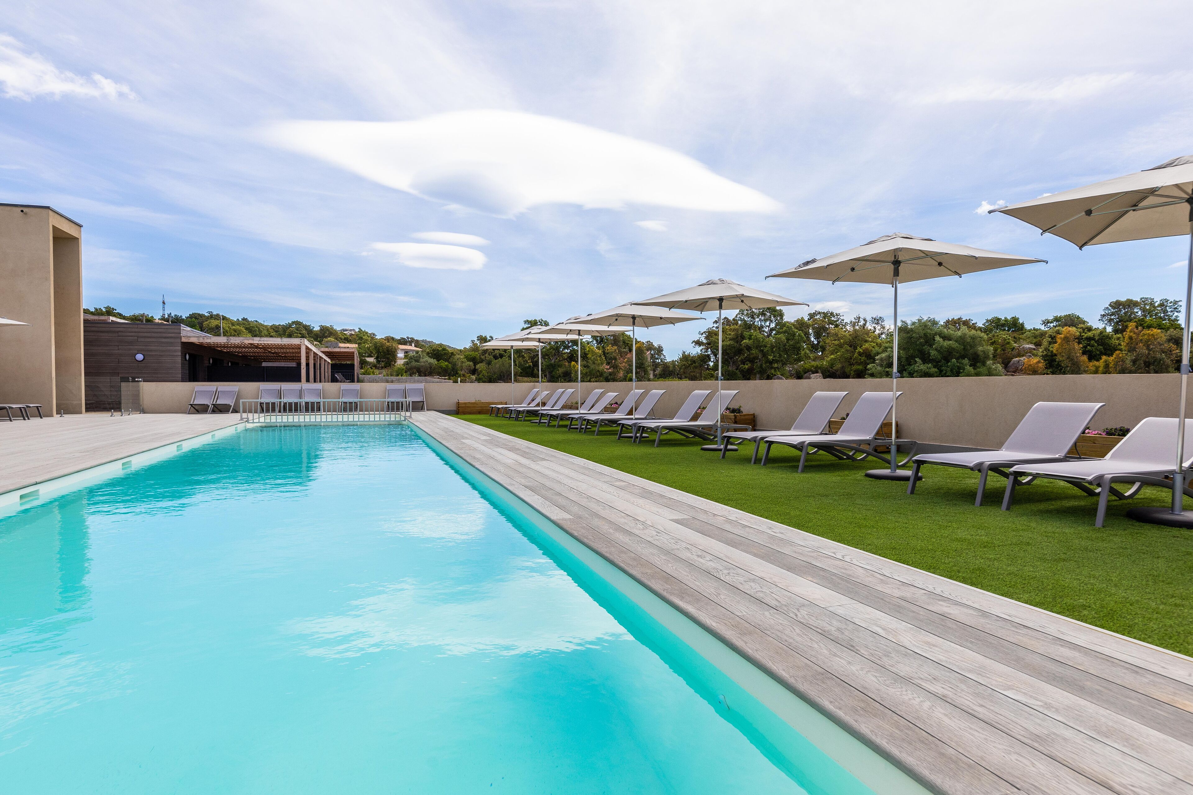 A swimming pool with lounge chairs and umbrellas, surrounded by a wooden deck and a grassy area.