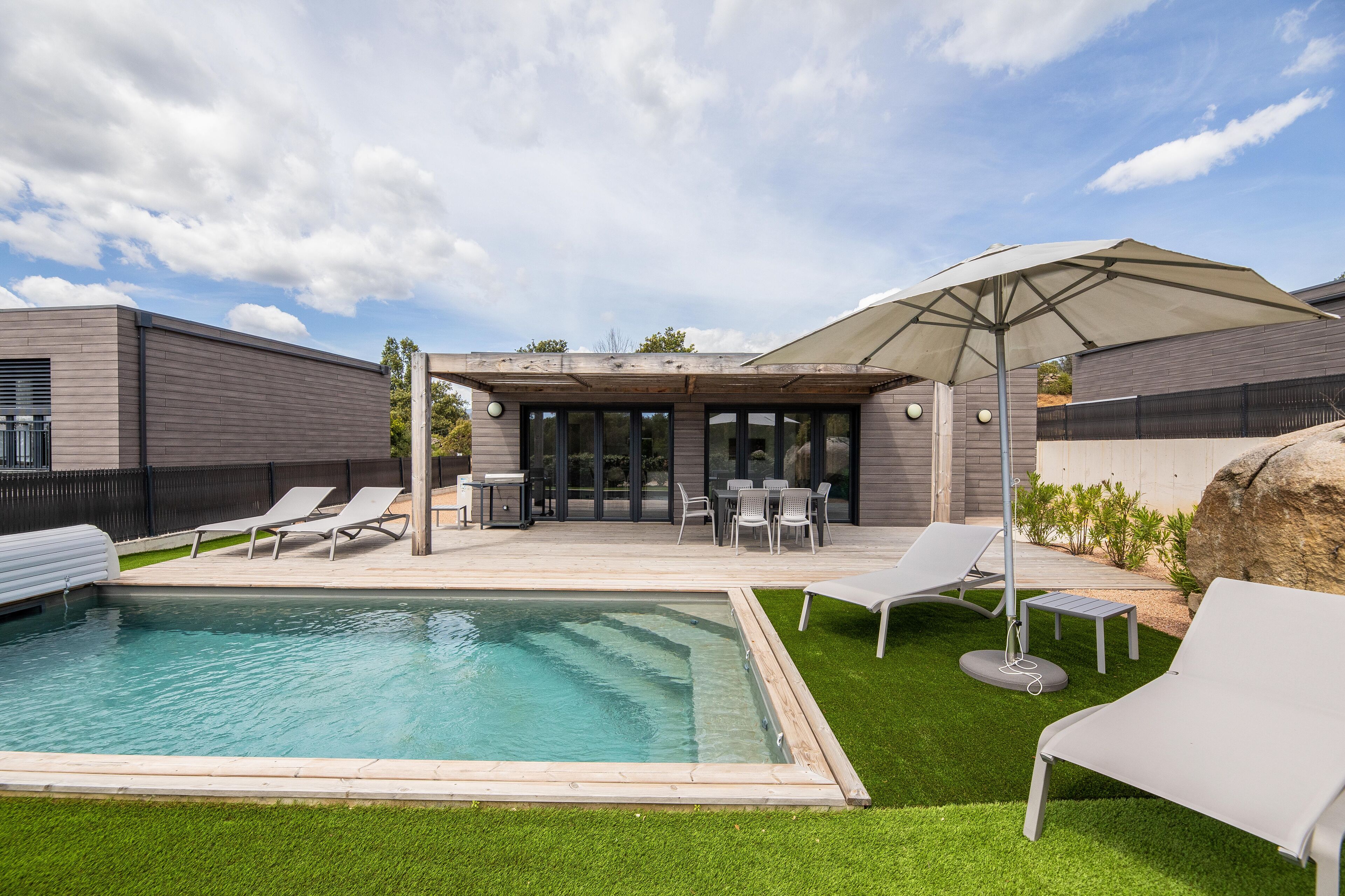 Un jardin moderne avec une piscine, des chaises longues et un espace patio couvert.