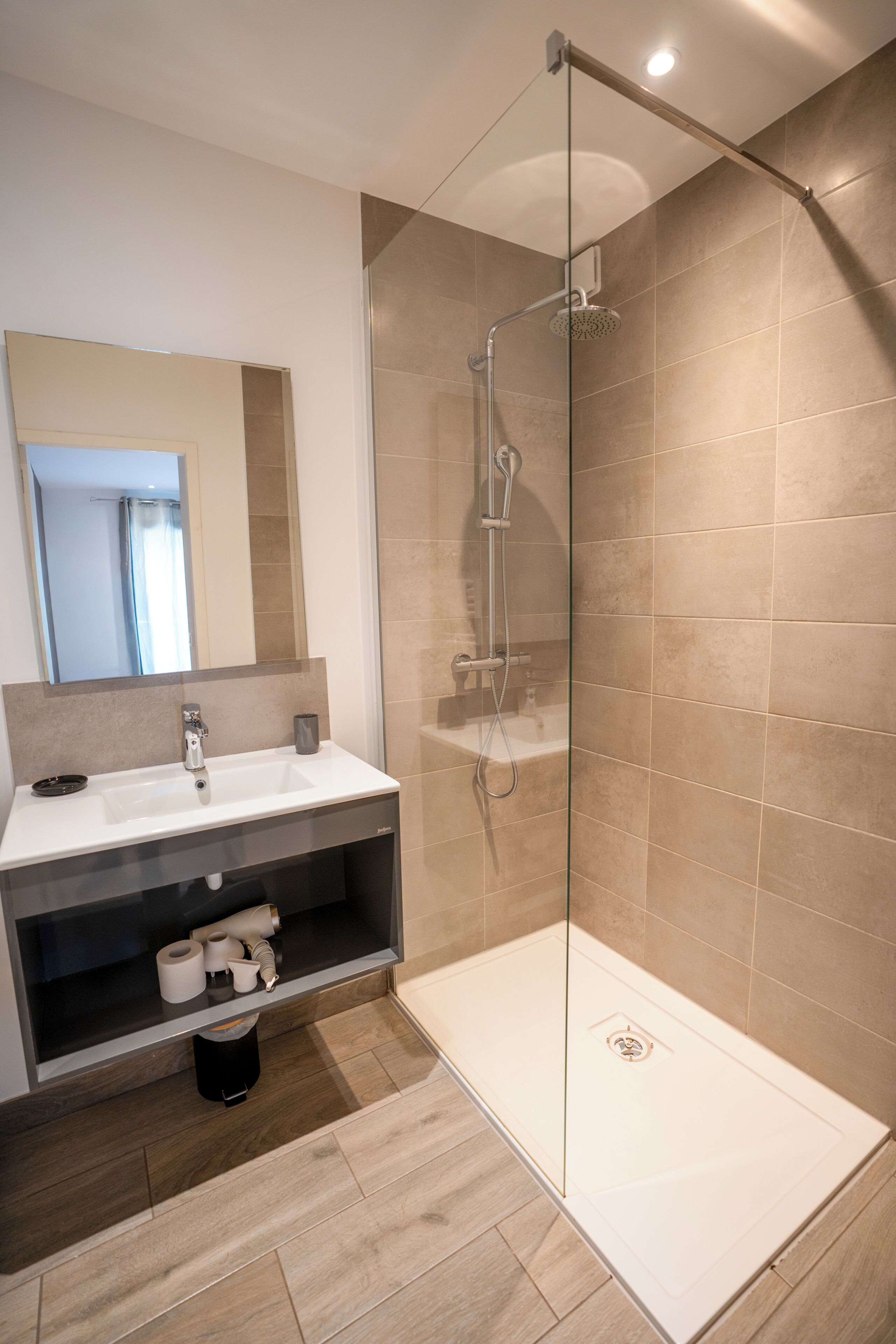 Ein modernes Badezimmer mit einer Duschkabine aus Glas, einem Waschbecken mit Spiegel und einem Ablagebereich für Toilettenartikel.
