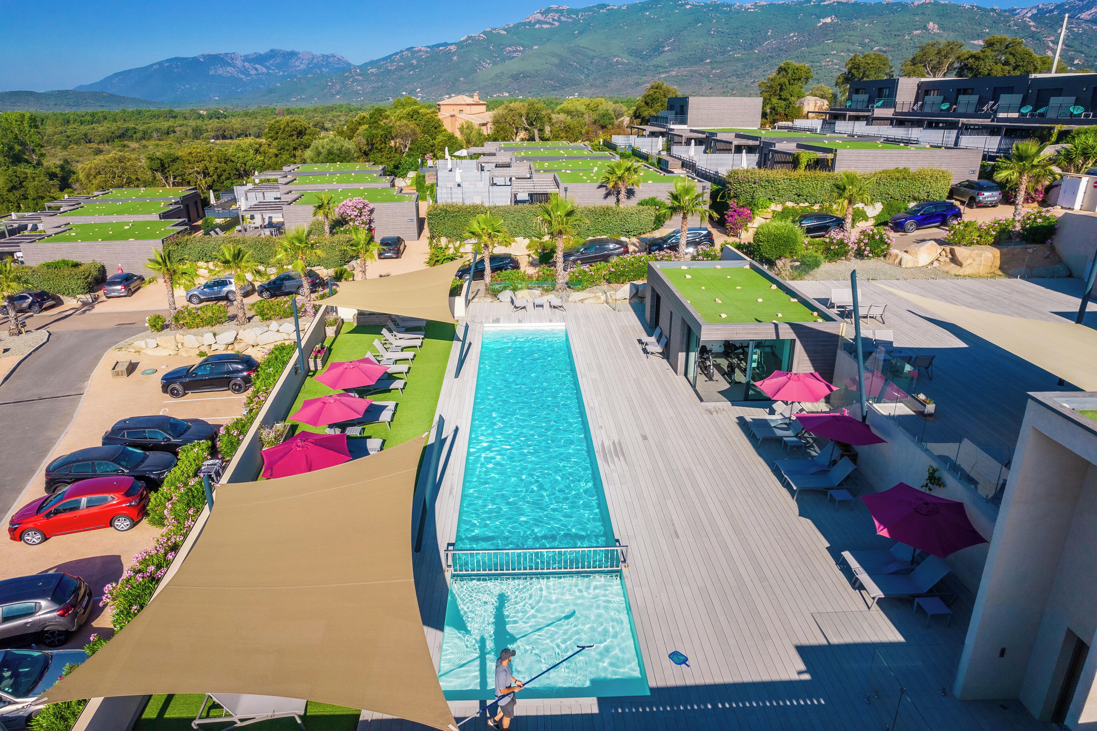 Una piscina en la azotea con vistas a montañas, rodeada de sillones de descanso y sombrillas.