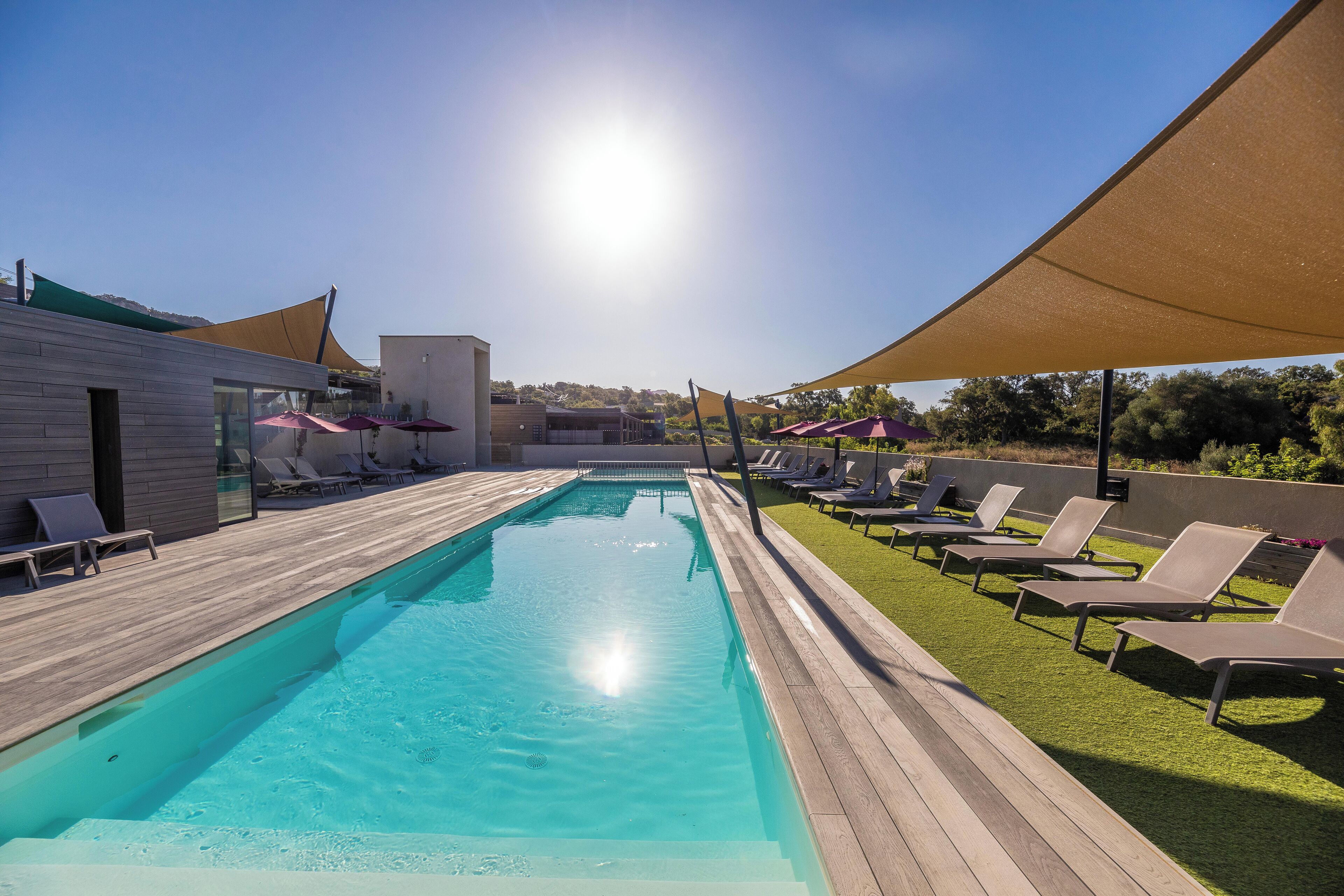 Une piscine dotée de structures ombragées, de chaises longues et d’une terrasse en bois.