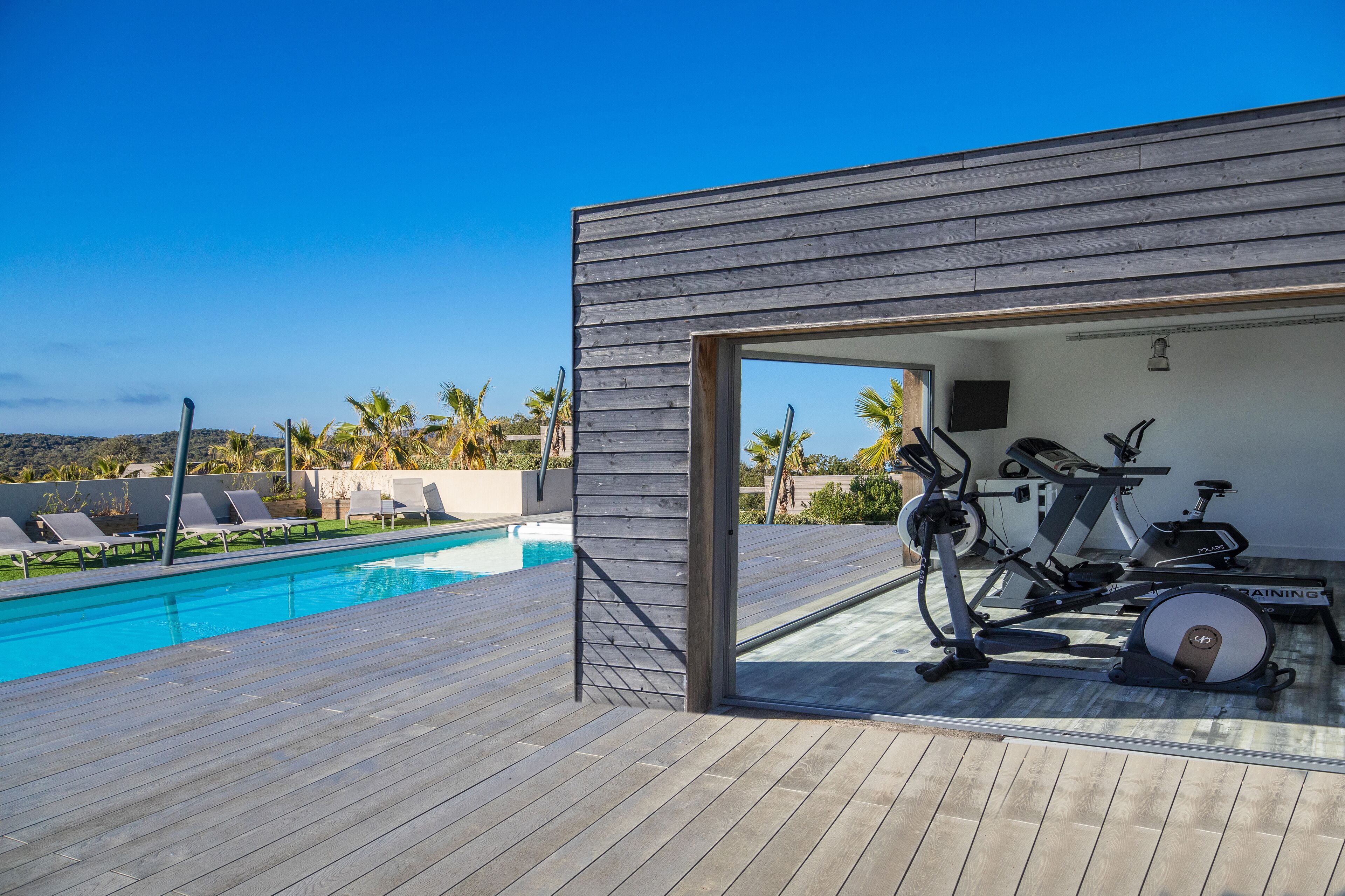 Ein moderner Außenbereich mit Holzterrasse, Schwimmbecken und Fitnessgeräten.