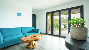 A modern living room with a blue sofa, a wooden coffee table, and a potted plant on a curved console table.