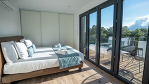 Ein Schlafzimmer mit Bett, einem Balkon mit Tisch und Stühlen sowie Blick auf Grünflächen.