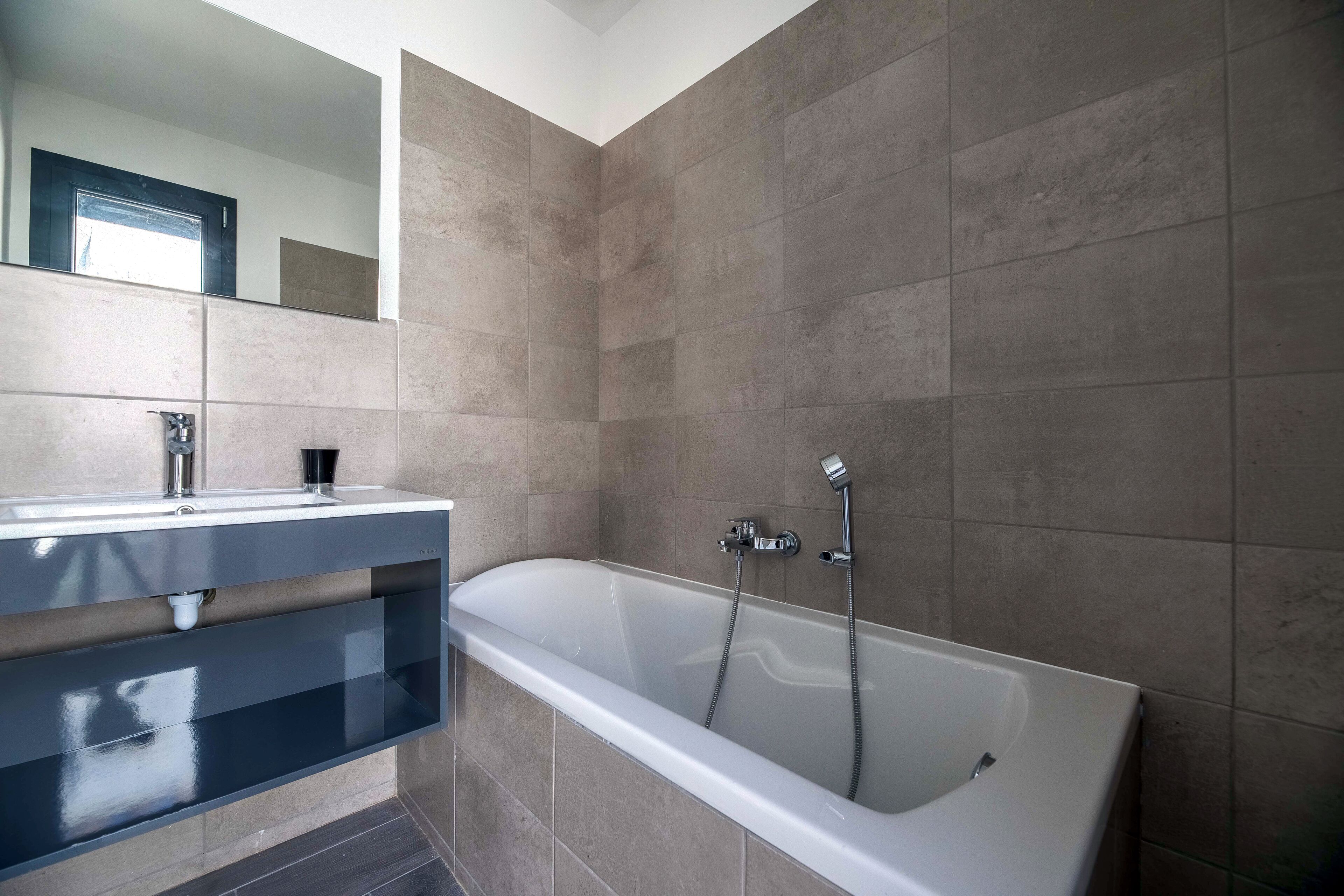 A modern bathroom with a bathtub, a vanity with a mirror, and tiled walls.
