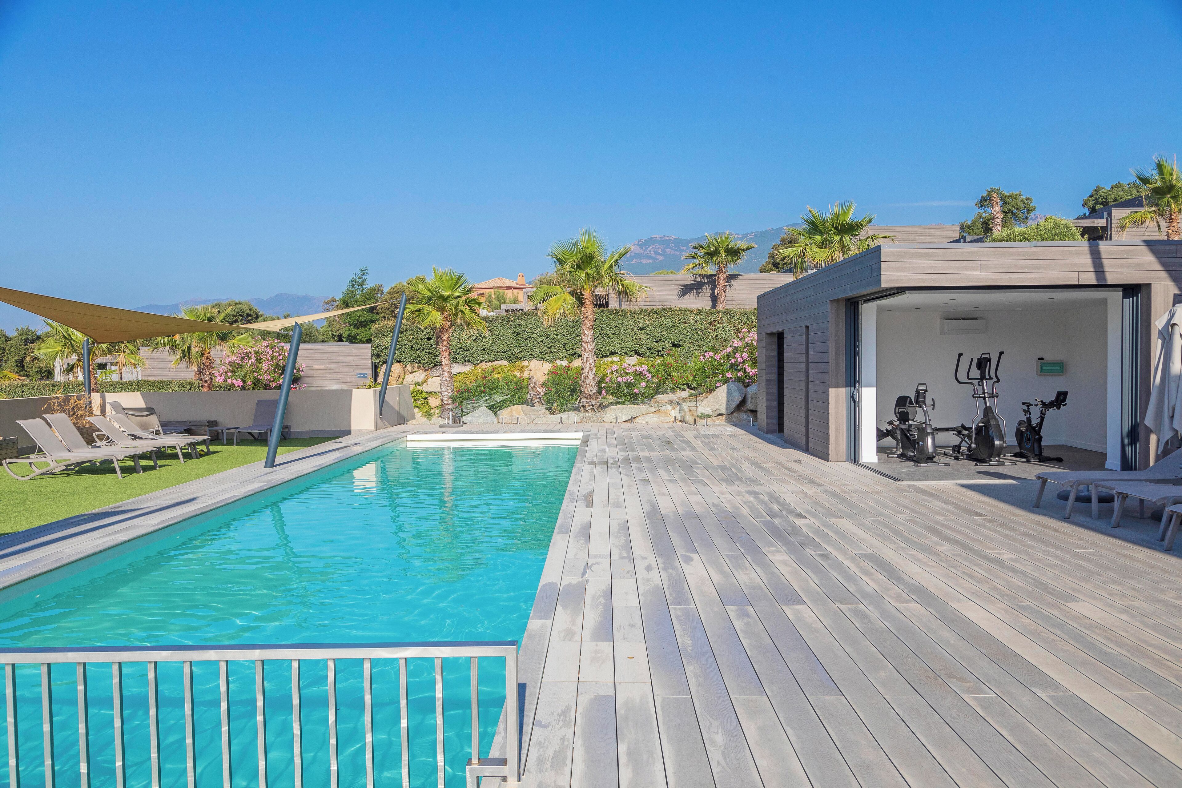 Una piscina con un pontile in legno, sedie a sdraio e cyclette.