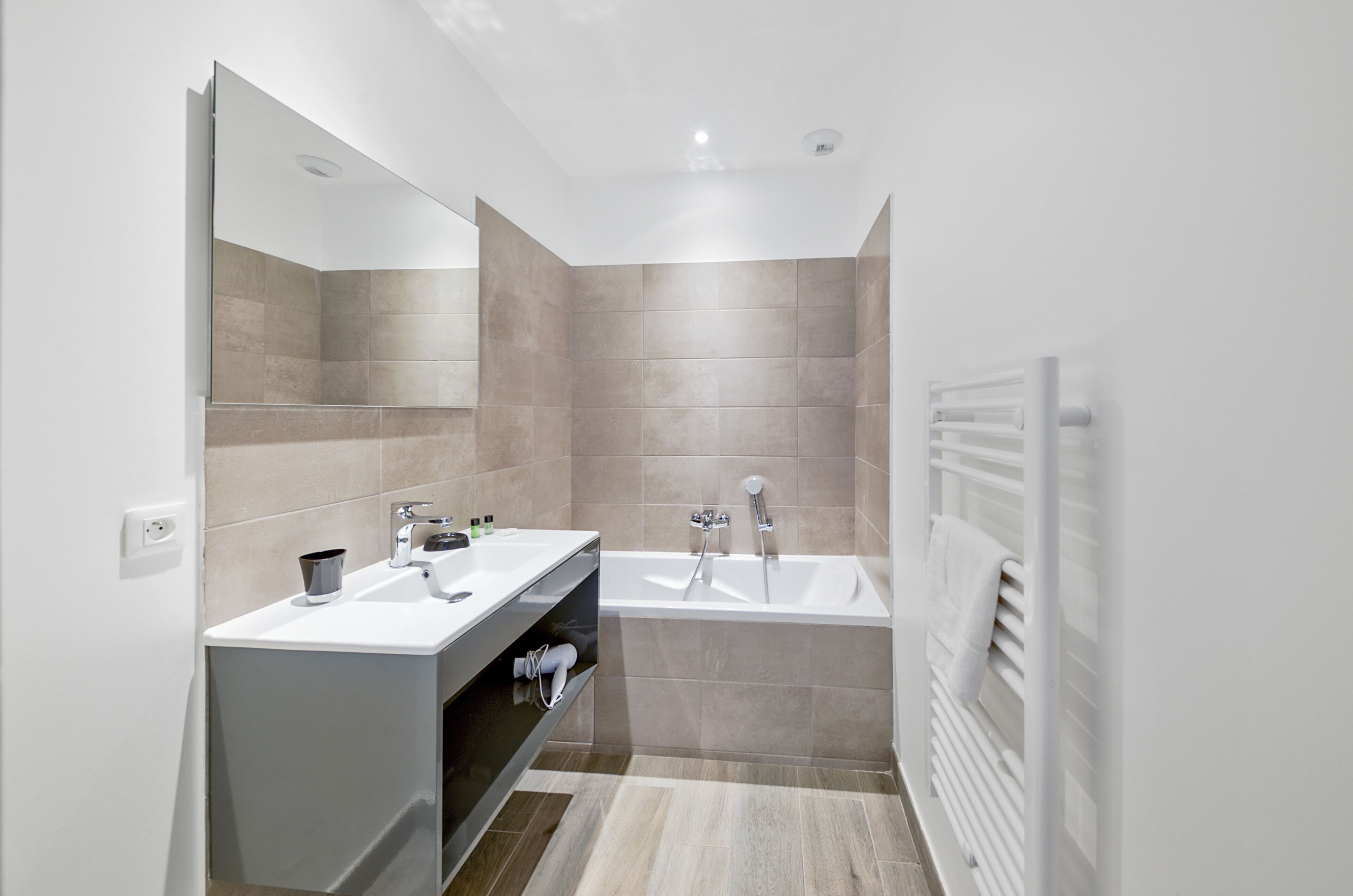 A modern bathroom with a large mirror, two sinks, a bathtub, and a towel rack.