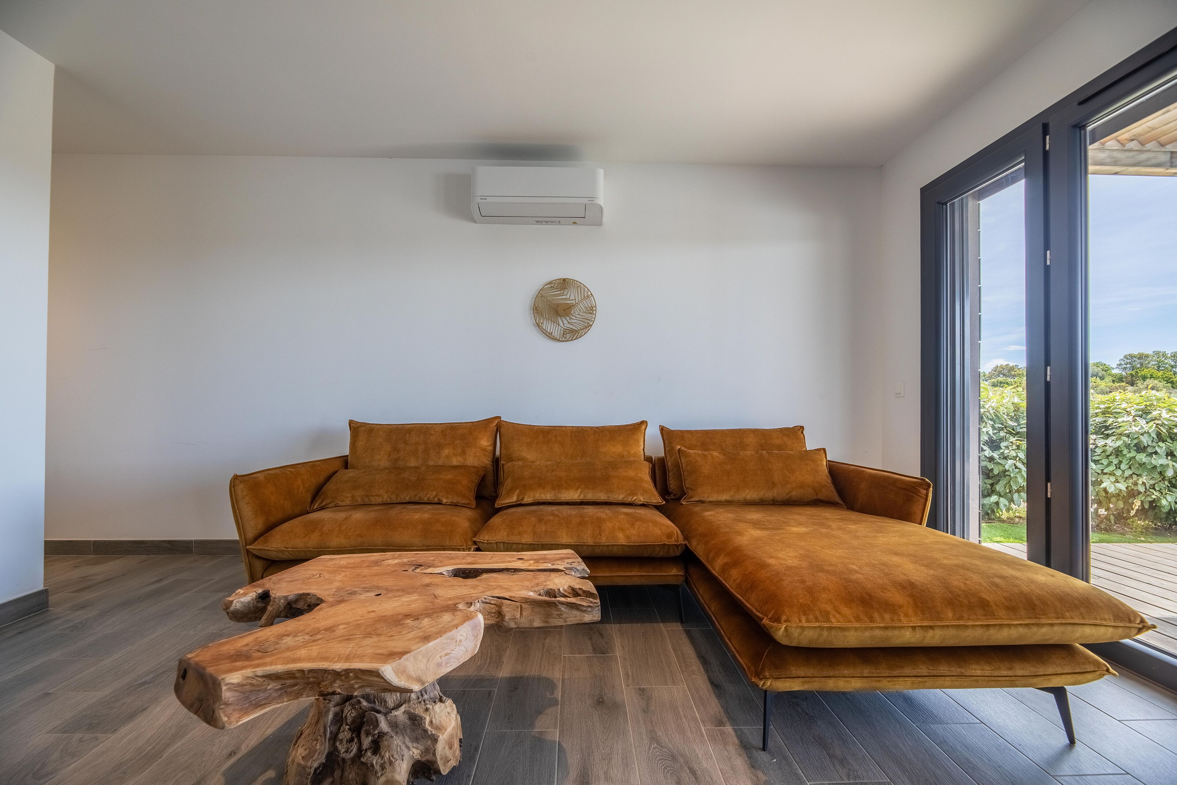 A modern living room with a sectional sofa, a wooden coffee table, and a large window offering a view of greenery.