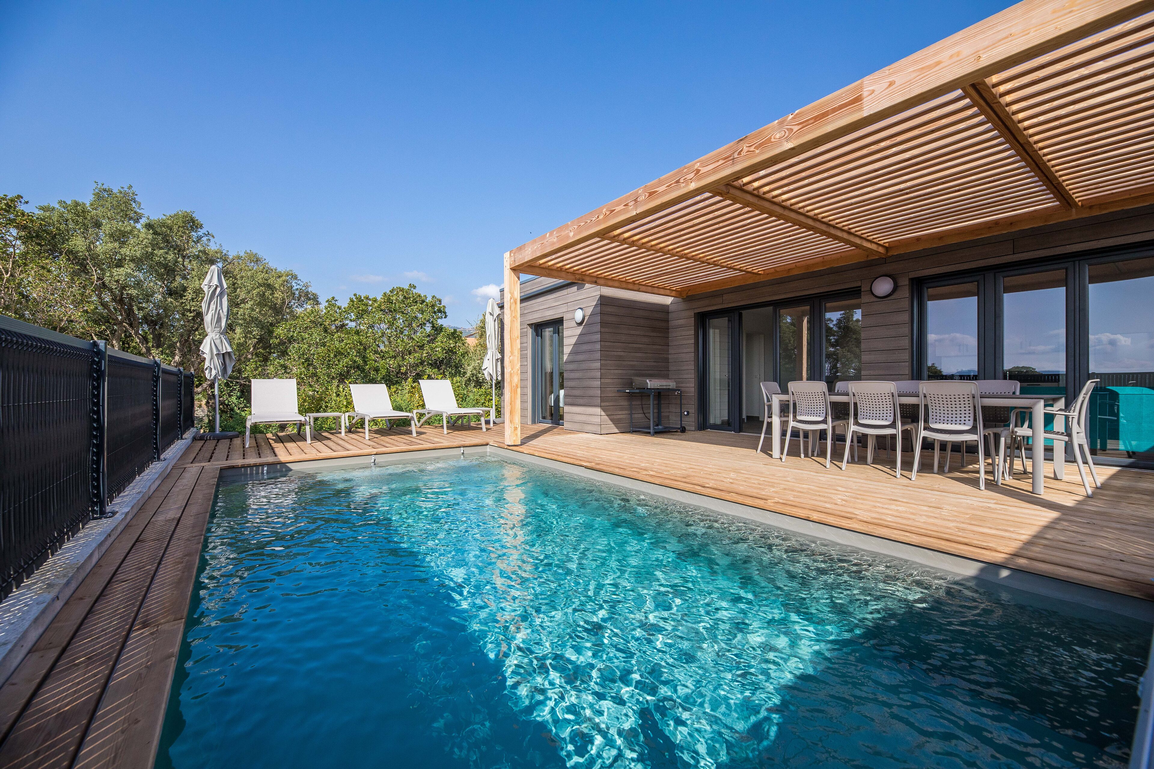 Une piscine avec une terrasse en bois, des chaises longues et un espace salon abrité.