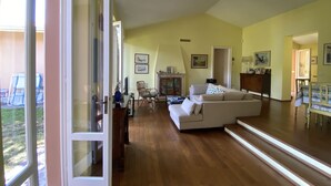 A spacious living room with a large sectional sofa, wooden flooring, and a view of the outdoors through a sliding glass door. - Gorgeous 9-seater villa, perfect for families with large garden by the lake (Bogliaco)